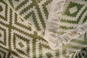 Macro detail of thick green geometric jacquard weave fabric with vintage fringe trim