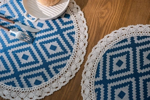 Detail of round woven placemat with blue geometric diamond pattern and lace border