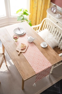 Detail of Nordic orange geometric jacquard table runner featuring white tassels on edges
