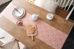 Close-up of geometric jacquard table runner in coral and cream on dark wood