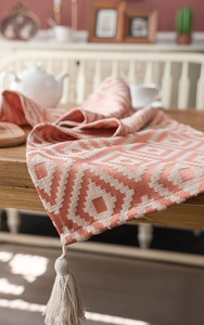 Close-up of orange geometric jacquard table runner fabric with decorative cream tassels