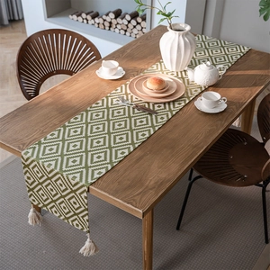 Green and white geometric jacquard table runner with tassels on a wooden dining table