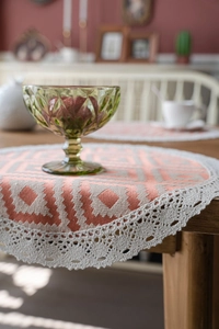 Detail of round orange woven placemat with intricate cream crochet lace edge trim