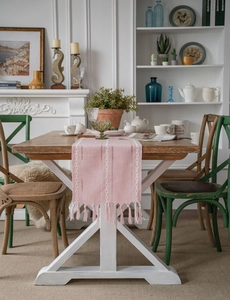 Pink table runner with white wave embroidery and tassels on a rustic dark wood table