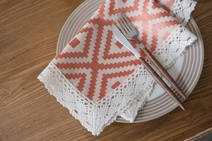 Close-up of orange geometric jacquard table runner with white lace edges on a ceramic plate