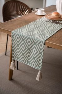 Detailed view of Nordic geometric green table runner with elegant cotton tassels on wood table