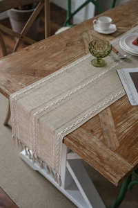 Close-up of beige jacquard table runner with white chain embroidery and handmade tassels