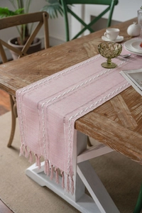Close-up of pink woven table runner featuring white handmade embroidery and tassels