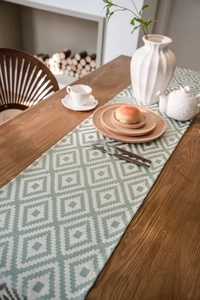 Detail of Nordic geometric green jacquard table runner with fringe on wood table