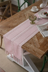 Detail of pink woven table runner with white textured patterns and elegant fringe
