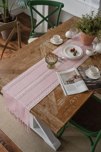 Detailed macro of pink cotton-linen table runner with chain embroidery and tassels