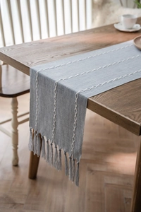 Detail of gray-blue linen-texture table runner with white geometric embroidery and tassels