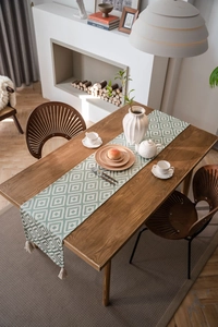 Detail of green and white geometric table runner with tassel on a wood dining table
