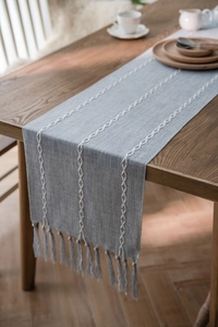 Detail of light blue Nordic table runner with white chain embroidery and tassel