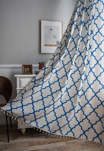 Detail of blue quatrefoil geometric print on off-white fabric curtain with fringe