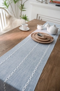 Detail view of light blue Nordic table runner with white leaf embroidery on wood table
