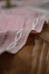 Close-up of pink Nordic table runner featuring white leaf embroidery and ladder stitch details