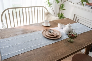Detail of light blue Nordic table runner with white geometric diamond embroidery on wood