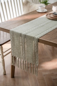 Detail of sage green jacquard table runner with woven white lines and fringe tassels