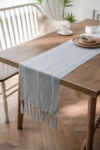 Close-up detail of blue woven table runner with white braided embroidery and fringe