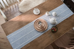 Detail of light blue jacquard table runner with white geometric embroidery on dark wood table