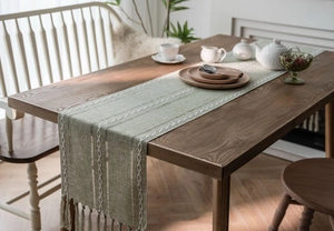 Close-up of sage green table runner with woven white stripes and elegant tassels