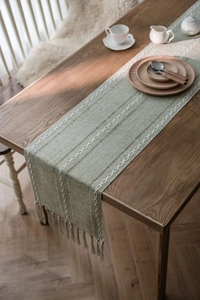 Close-up of sage green woven table runner with white textured stripes and tassels