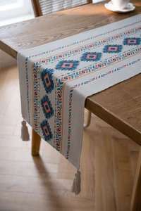 Detail of bohemian table runner with geometric orange blue patterns and white tassels