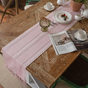 Pink jacquard table runner with white chain embroidery and tassels on a wooden table