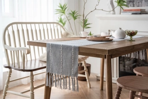 Close-up of gray-blue table runner with white woven stripes and elegant fringe details