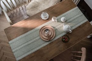 Close-up of sage green jacquard table runner with white woven fringe on a wooden table