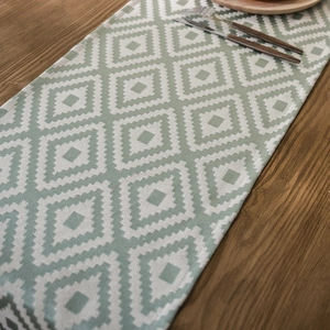 Nordic green and white geometric diamond table runner with woven texture on wood table