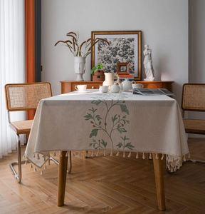 Detail view of cream cotton linen tablecloth with green floral embroidery and tassels