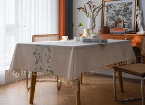 Close-up of cream linen tablecloth featuring floral embroidery and elegant fringe tassels
