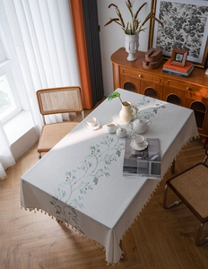 Detail of floral embroidery and fringe trim on rectangular beige rustic tablecloth