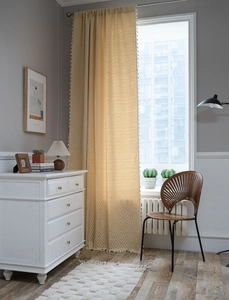 Detailed view of yellow jacquard curtain with diamond patterns and white tassel fringe
