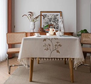 Close-up of elegant floral embroidery and cotton tassels on cream linen tablecloth