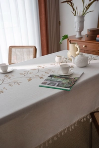 Close-up of golden floral embroidery on linen-textured tablecloth with elegant fringe