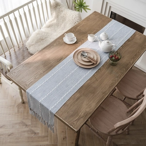 Nordic light blue table runner with white chain embroidery and tassels on wooden table