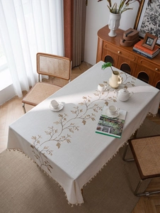 Detailed embroidery of brown floral branches on cream cotton linen tablecloth with tassels