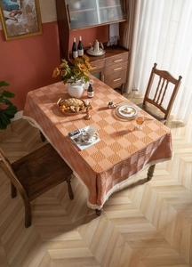 Detailaufnahme der orangefarbenen Tischdecke mit Karomuster und dekorativen weißen Quasten
