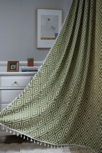 Detail of green geometric pattern curtain with white tassels in a cozy home setting