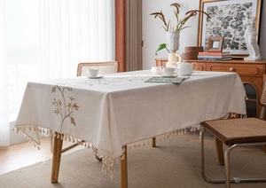 Close-up of beige linen tablecloth featuring brown floral embroidery and fringe tassel edges