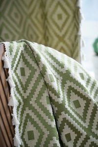 Close-up of green diamond pattern woven curtain with decorative white cotton fringe