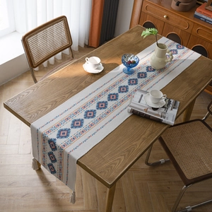 Bohemian table runner with geometric diamond patterns and fringe on a wooden dining table