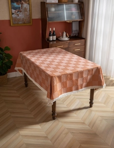Detail der karierten orange-beigen Tischdecke mit Quastenrand auf einem Holztisch
