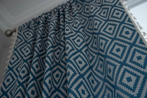 Close-up of blue geometric diamond jacquard curtain fabric with decorative tassels