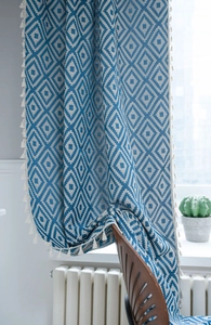 Detail of blue and white geometric diamond pattern curtain fabric with white fringe tassels