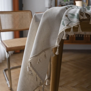 Linen table runner with green leaf embroidery and beige fringe on wooden dining table