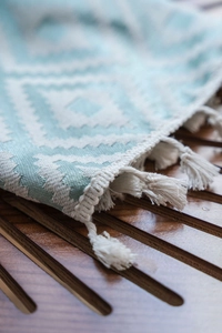 Detail of woven geometric cotton runner with white fringes on dark wood tray